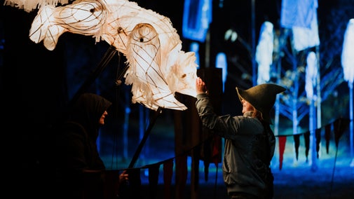 A child in a hat strokes a large, illuminated fox puppet.